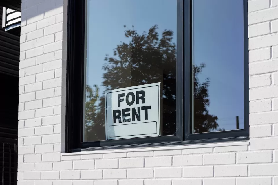 For Rent sign in window on white tiled wall.